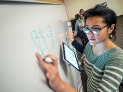 Student with glasses practicing writing Chinese on a white board in class.